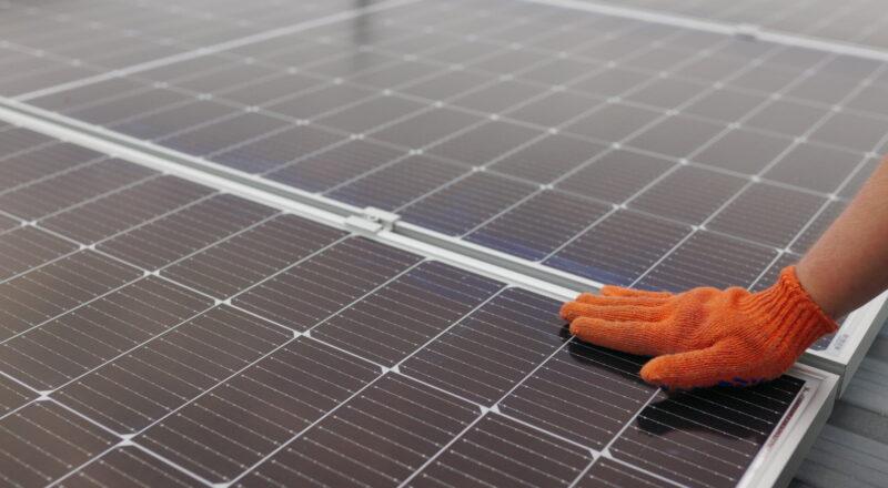 Nahaufnahme einer Hand, die den Betrieb, die Sauberkeit und Oberfläche von Photovoltaik-Solarmodulen überprüft